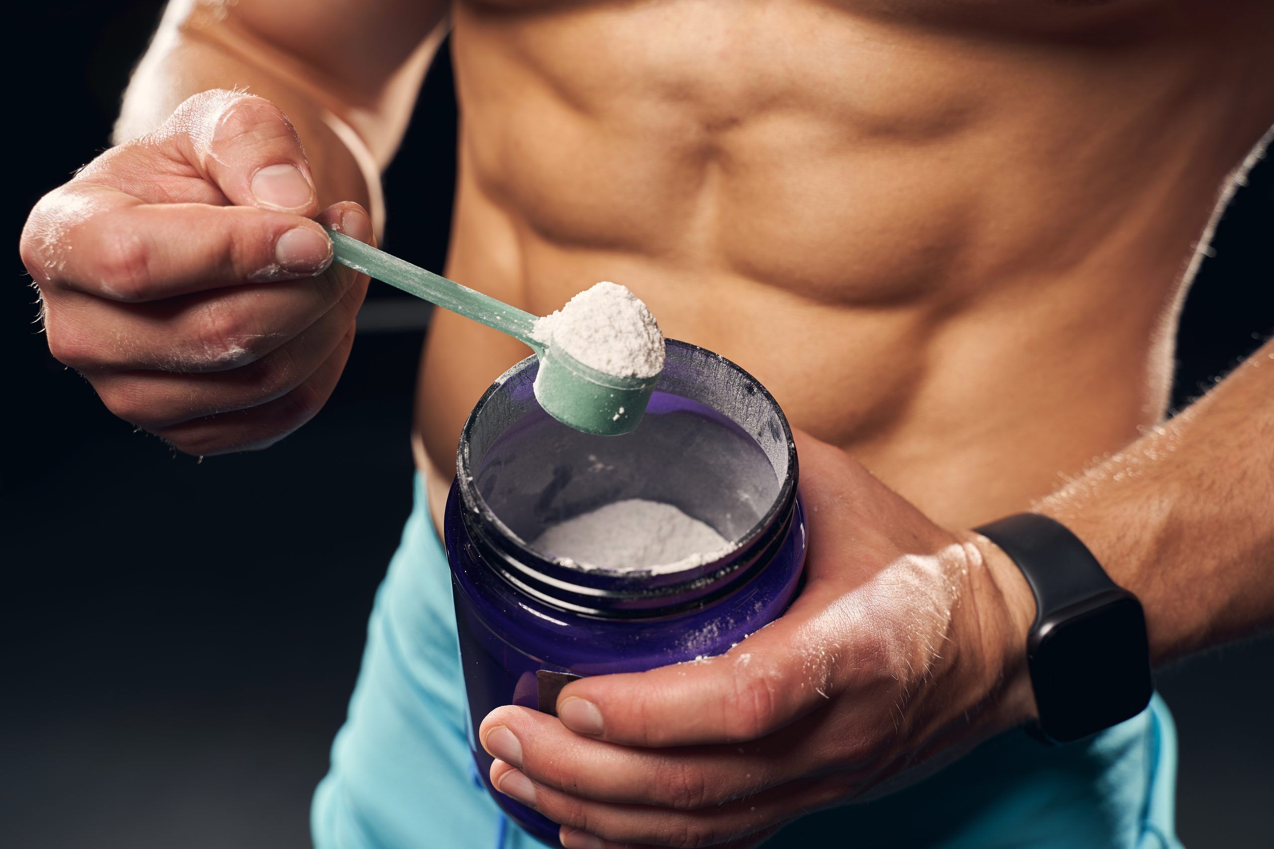 shirtless muscly man wearing sport shorts scooping powder protein from jar scaled ec8a9f3b